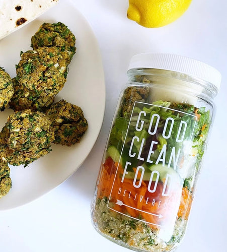 Jar labeled 'Good Clean Food Delivered' with salad ingredients, next to a plate of falafel.