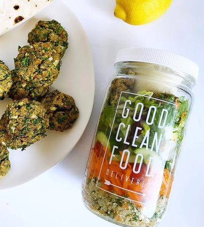 Jar labeled 'Good Clean Food Delivered' with salad ingredients, next to a plate of falafel.